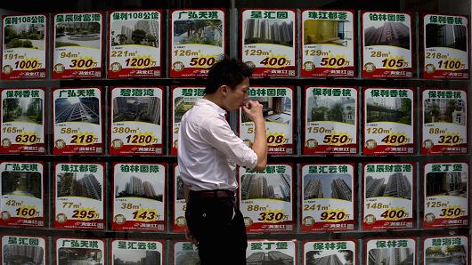 A man walks in front of advertisements for residential property in the glass facade of a real estate agency in Guangzhou, Guangdong province of China.
