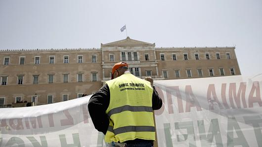 A protestor holds a banner outside the Greek parliament during in a demonstration by municipal contract workers in Athens, Greece, on Thursday, June 29, 2017.