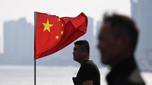 Two Chinese men stand near a Chinese flag as they look out towards North Korea while visiting the Broken Bridge, in the Chinese border city of Dandong, in China's northeast Liaoning province on September 5, 2017.