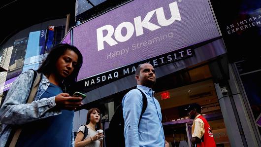 People pass by a video sign display with the logo for Roku Inc, a Fox-backed video streaming firm, that held it's IPO at the Nasdaq Marketsite in New York, U.S., September 28, 2017.