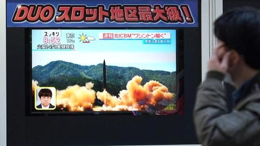 A pedestrian walks in front of a television screen displaying file news footage of a North Korean missile launch, in Tokyo on November 29, 2017
