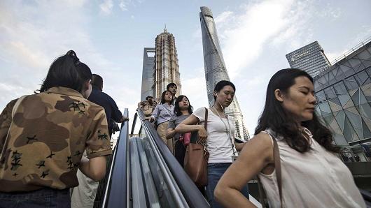 Pedestrians ride an escalator near the Jin Mao Tower, center left, and the Shanghai Tower, center right, in the Lujiazui Financial District in Shanghai, China.