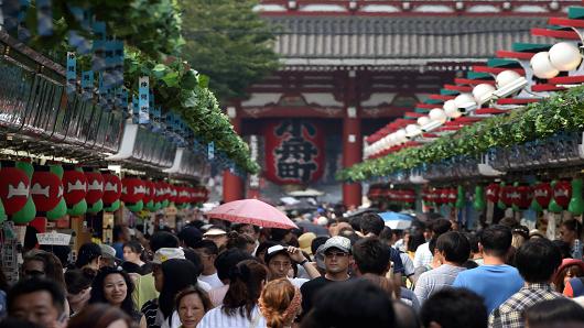 Shoppers and tourists walk through a shopping street in front of the Sensoji temple in Tokyo, Japan, on Thursday, Aug. 8, 2013.