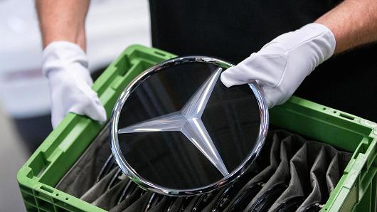 An employee holds a Mercedes-Benz badge on the assembly line at the automaker's factory in Bremen, Germany.