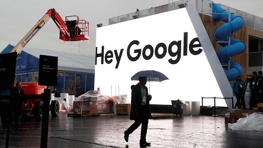 A man walks through light rain in front of the Hey Google booth under construction at the Las Vegas Convention Center in preparation for the 2018 CES in Las Vegas, Nevada, January 8, 2018.