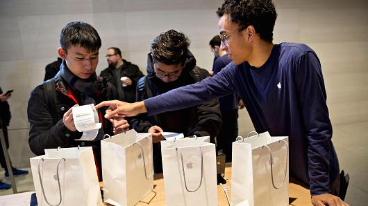 An employee assists a customer who purchased four Apple Inc. iPhone X smartphones during the sales launch at a store in Chicago.