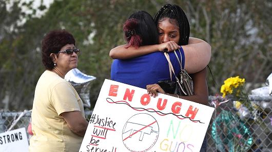 Tyra Heman (R) a senior at Marjory Stoneman Douglas High School, holds a sign that reads, 'Enough No Guns,' as she is hugged in front of the school where 17 people that were killed on February 14, on February 19, 2018 in Parkland, Florida.