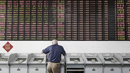 An investor stands at a trading terminal in front of an electronic stock board at a securities brokerage in Shanghai, China, on Friday, June 9, 2017.
