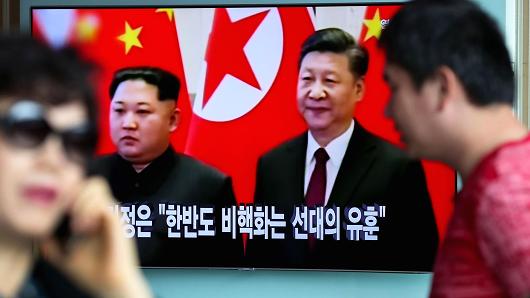 People walk past a television screen showing a news broadcast, featuring North Korean Leader Kim Jong Un during a meeting with with China's president Xi Jinping, at Seoul Station in Seoul, South Korea, on Wednesday, March 28, 2018.