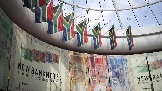 South African national flags hang above an advertisement for the new Mandela rand banknotes at the headquarters of the central bank in Pretoria, South Africa, on May 23, 2013.