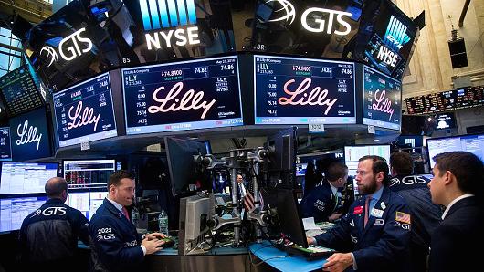 Traders work beneath monitors displaying Eli Lilly & Co. signage on the floor of the New York Stock Exchange (NYSE) in New York, U.S., on Monday, May 23, 2016.