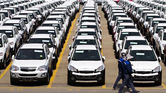 Workers walk past parked General Motors Co. (GM) Chevrolet automobiles bound for export at the Port of Incheon in Incheon, South Korea.