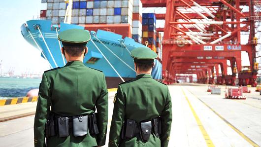 Police officers are seen in front of a cargo ship with containers at a port in Qingdao, Shandong province, China April 6, 2018.