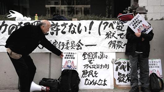 People gathering near the Japan Parliament hold placards against Japanese Prime Minister Shinzo Abe as Yasunori Kagoike, head of the Moritomo Gakuen group, gives sworn testimony in the Diet on March 23, 2017.