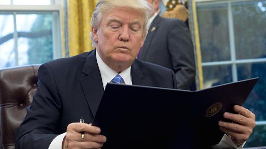 President Donald Trump reads an executive order withdrawing the US from the Trans-Pacific Partnership prior to signing it in the Oval Office of the White House in Washington, DC, January 23, 2017.