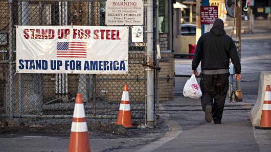 A man walks past a 'Stand Up For Steel, Stand Up For America' sign while arriving at the United States Steel Corp. Clairton Plant coke manufacturing facility as emissions rise in Clairton, Pennsylvania.