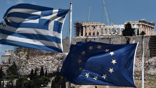 An EU and a Greek flag wave in front of the ancient temple of Parthenon atop the Acropolis hill in Athens.