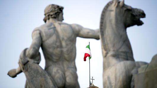 The Italian national flag, seen between statues, flies atop the Quirinale palace, the office of Italy's president in Rome, Italy.