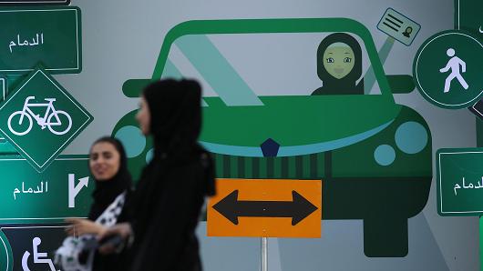 Young women wearing the traditional abaya walk past a sign as they help to organize an outdoor educational driving event for women on June 21, 2018 in Jeddah, Saudi Arabia.
