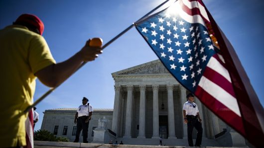 A person waves an American flag outside the the U.S. Supreme Court building as the court rules on the final opinions of term in Washington, D.C., on Monday, June 25, 2018.