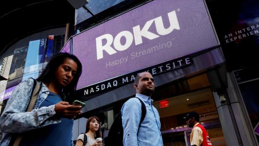 People pass by a video sign display with the logo for Roku, a Fox-backed video streaming firm, that held it's IPO at the Nasdaq Marketsite in New York, September 28, 2017.