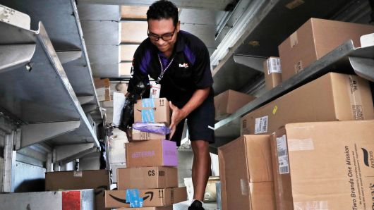 In this Tuesday, July 17, 2018 photo, a FedEx employee delivers packages in Miami. 