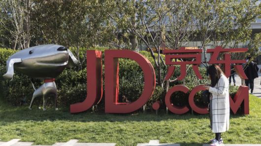 A woman stands next to signage incorporating the logo of JD.com, and the company's mascot 'Joy,' at the company's headquarters in Beijing, China.
