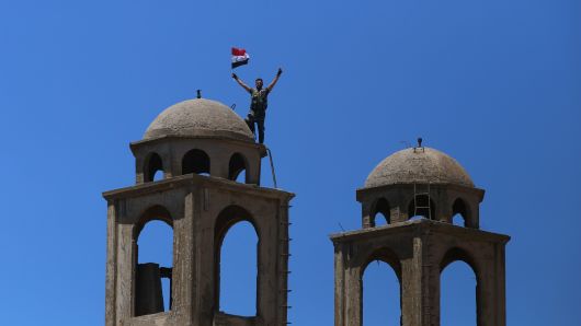 A Syrian soldier waves the national flag atop the Greek Orthodox Church of St. George in the town of Quneitra in the Syrian Golan Heights on July 27, 2018. - The town was almost completely destroyed by departing Israeli soldiers in 1974 after seven years of occupation.