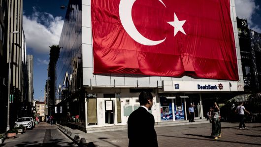 Pedestrians pass a giant Turkish national flag hanging above a DenizBank AS bank branch in Istanbul, Turkey, on Tuesday, July 19, 2016. Turkey's central bank slowed the pace of interest rate cuts at its meeting on Tuesday after the failed coup attempt triggered a sell-off in the currency and sovereign debt. 