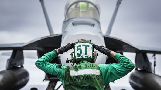 U.S. Navy Aviation Electronics Technician signals to the crew of an EA-18G Growler on the flight deck of aircraft carrier USS Carl Vinson.