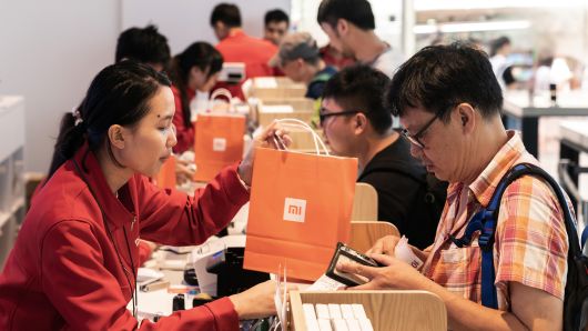 An employee, left, hands a Xiaomi Corp. branded shopping bag to a customer inside a Xiaomi store. 