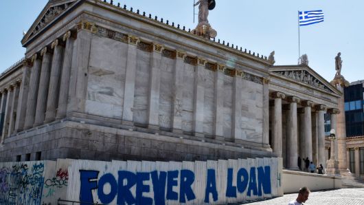 A woman walks past a graffiti refering to the Greek debt and reading 'Forever a loan' outside the Academy of Athens building on August 28, 2017.