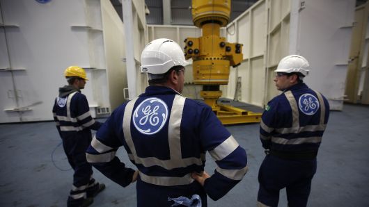 Employees stand as a subsea oil and gas tree is maneuvered by a crane at the General Electric Co. (GE) manufacturing plant in Montrose, U.K.