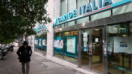 A pedestrian passes a Banca Carige SpA bank branch in Rome, Italy.
