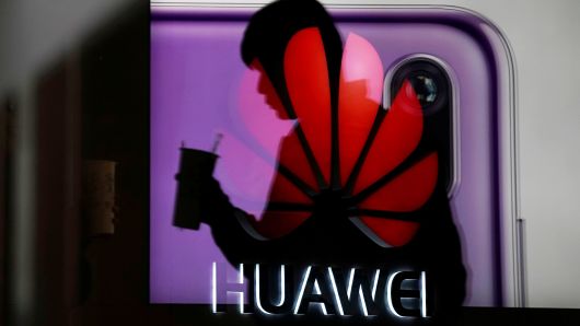 A man walking past a Huawei P20 smartphone advertisement is reflected in a glass door in front of a Huawei logo, at a shopping mall in Shanghai, China December 6, 2018. 