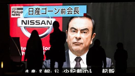 Pedestrians walk in front of a monitor showing an image of former Nissan Motor Co. Chairman Carlos Ghosn in a news program on December 10, 2018 in Tokyo, Japan. 