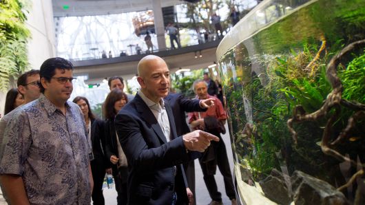 Jeff Bezos, founder and chief executive officer of Amazon points to an aquarium while touring the Spheres during opening day ceremonies at the company's campus in Seattle, Washington, in 2018. The Spheres, a new gathering and working space for Amazon employees located in the heart of the downtown Seattle Amazon campus, contains hundreds of plant species and maintains a tropical climate similar to Costa Rica.