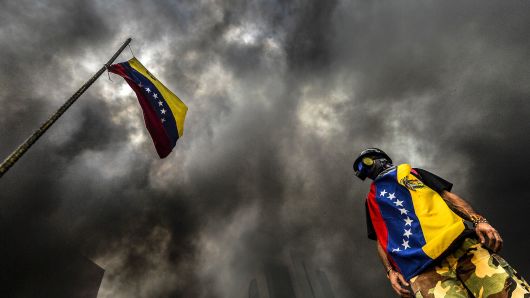 An anti-government demonstrator stands next to a national flag during an opposition protest blocking the Francisco Fajardo highway in Caracas on May 27, 2017.