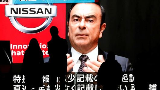 Passersby are silhouetted as a huge street monitor broadcasts news reporting ousted Nissan Motor chairman Carlos Ghosn's indictment and re-arrest in Tokyo, Japan December 10, 2018.