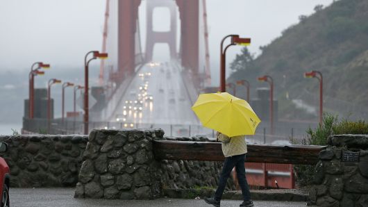 A woman walks in the rain at a vista point with the Golden Gate Bridge in the background Monday, Jan. 8, 2018, near Sausalito, Calif. Storms brought rain to California on Monday and increased the risk of mudslides in fire-ravaged communities in devastated northern wine country and authorities to order evacuations farther south for towns below hillsides burned by the state's largest-ever wildfire.