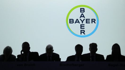 The Bayer AG logo sits behind silhouetted members of the management board during the company's annual general meeting in Bonn, Germany, May 25, 2018.
