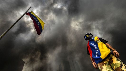 An anti-government demonstrator stands next to a national flag during an opposition protest blocking the Francisco Fajardo highway in Caracas on May 27, 2017.